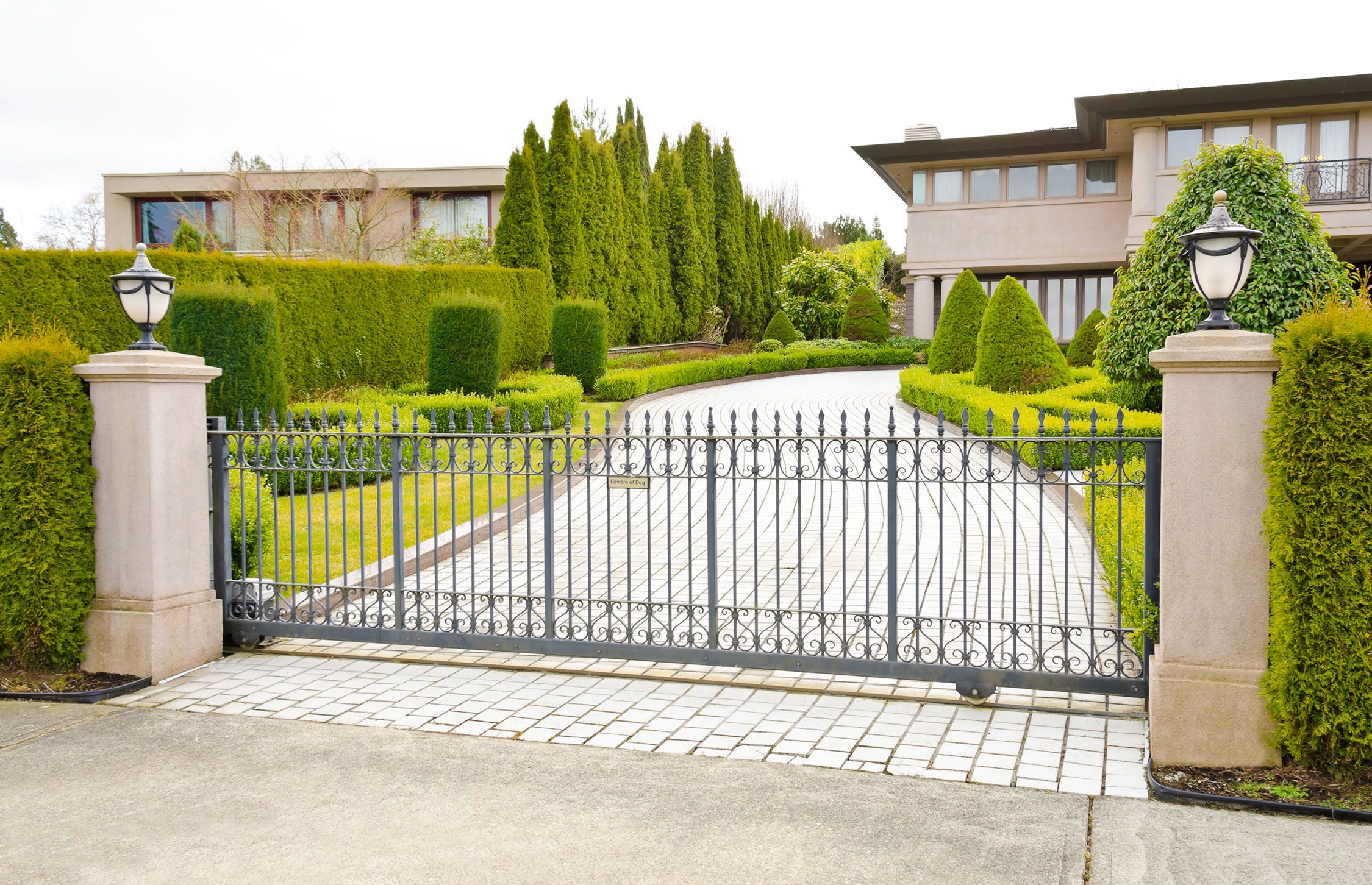 gated entry to mansion with shrubbery lining driveway