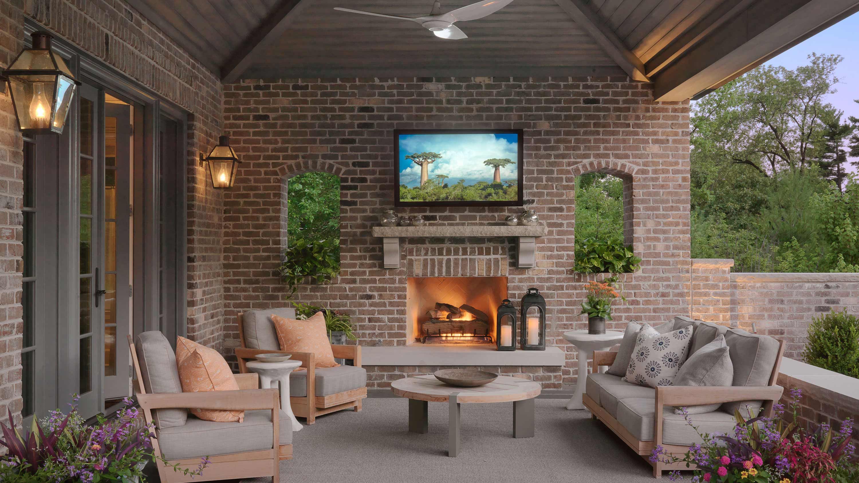 Patio with brick, tv on wall, grey chairs with peach pillows